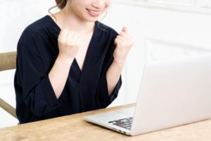 女性がパソコンの前でガッツポーズをしている